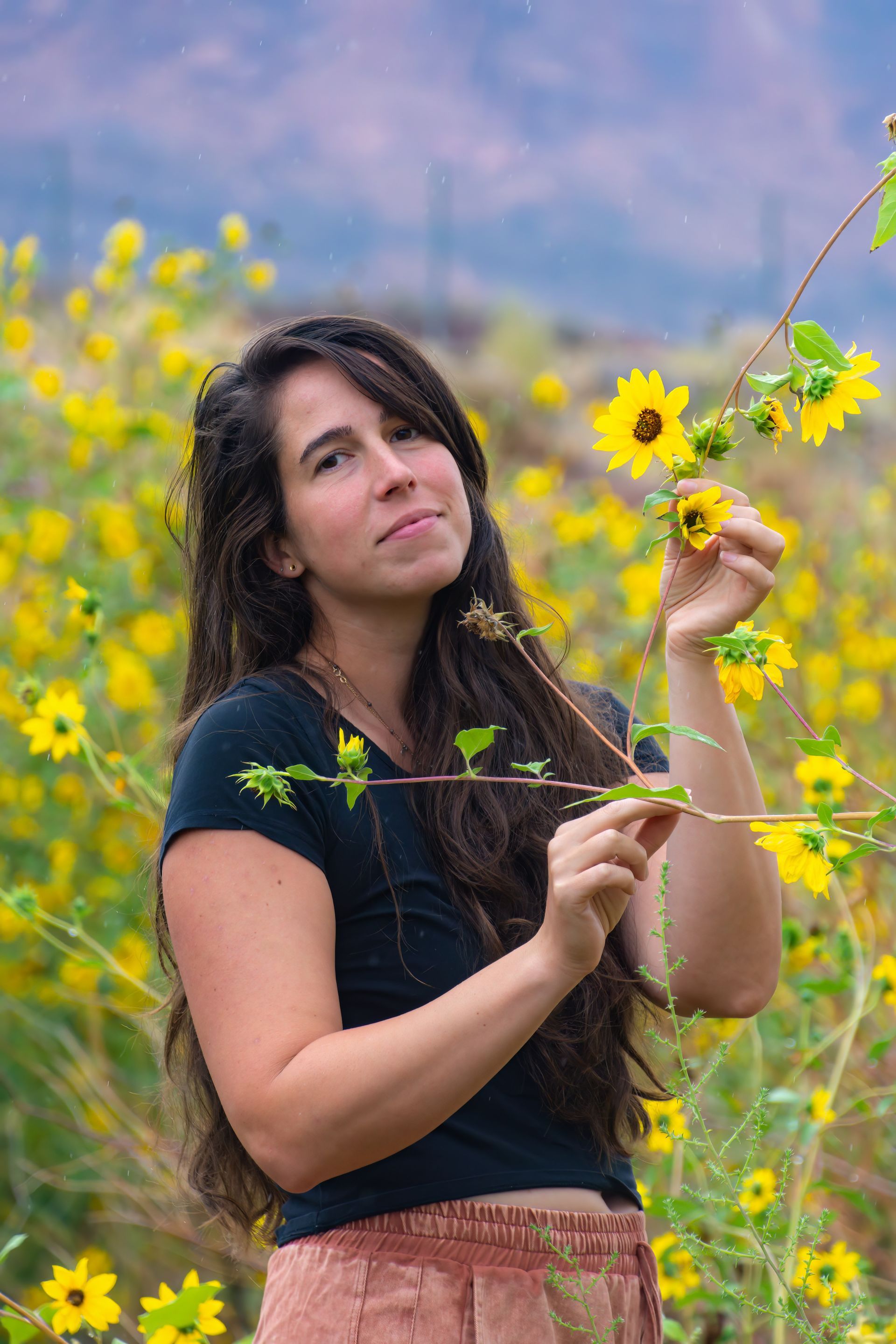 A woman is standing in a field of yellow flowers.