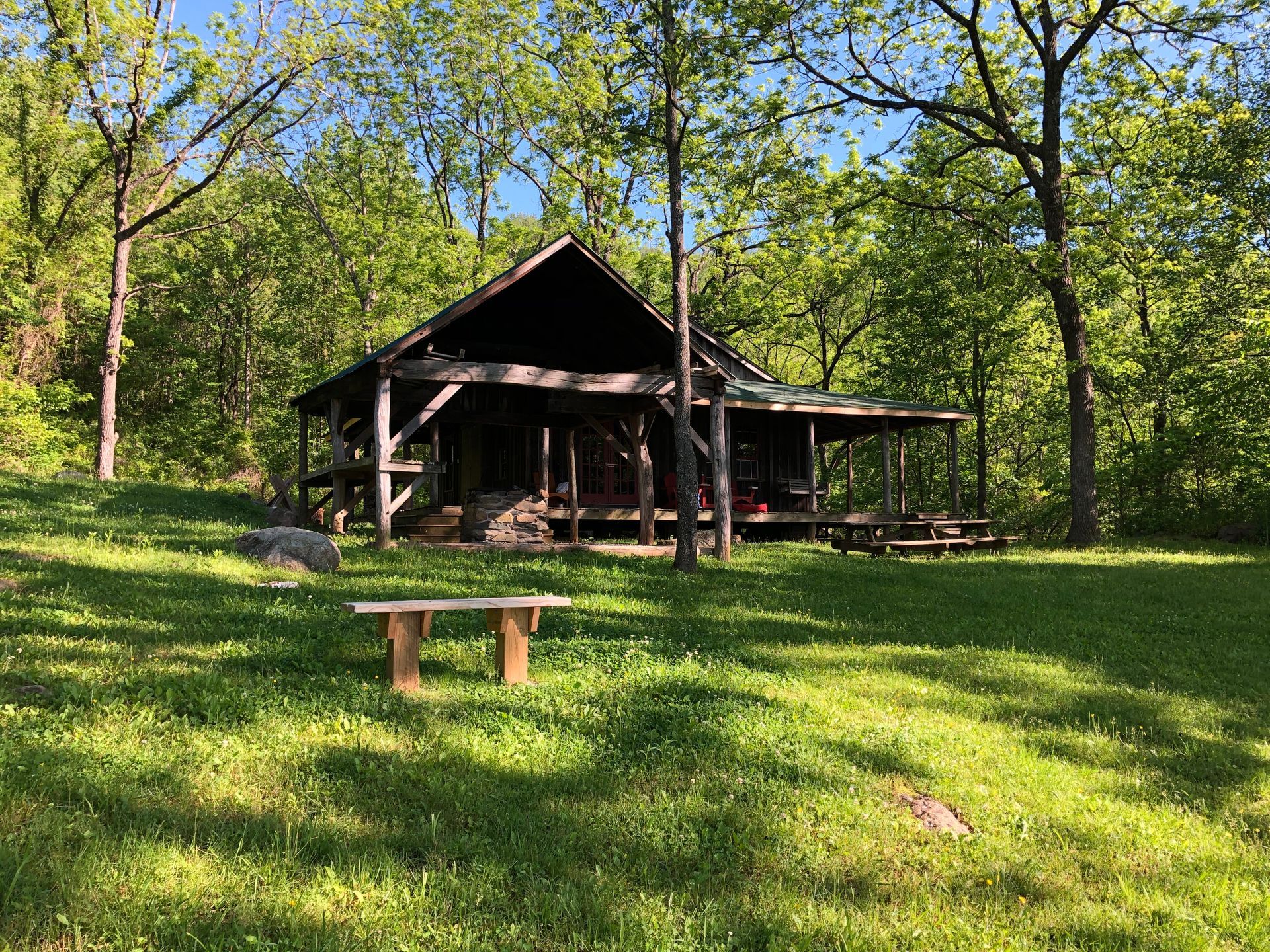 A wooden cabin is sitting in the middle of a grassy field surrounded by trees.