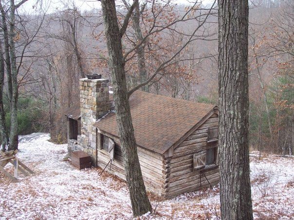 A small log cabin with a picnic table in front of it in the woods.