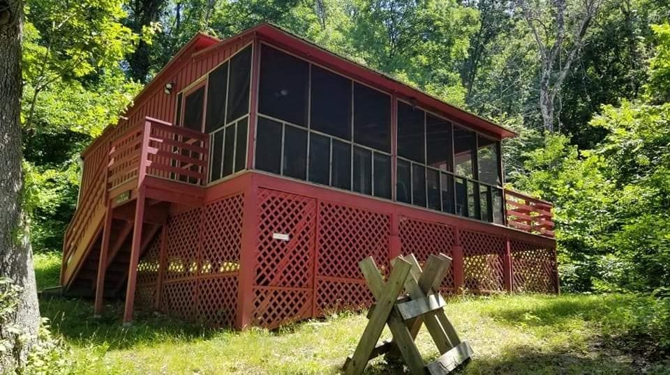 A red house with a screened in porch is surrounded by trees.