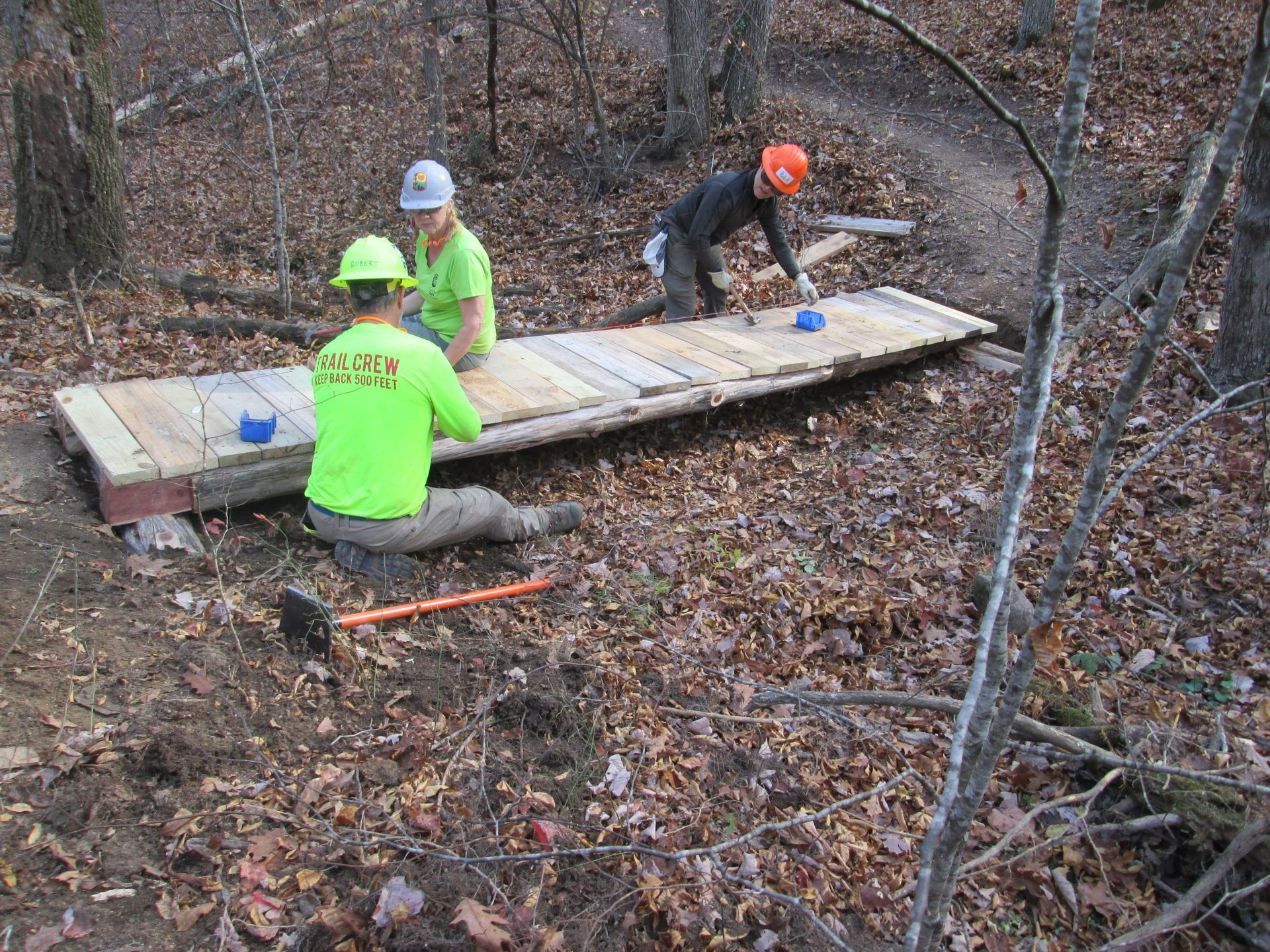 Two men are working on a wooden platform in the woods.