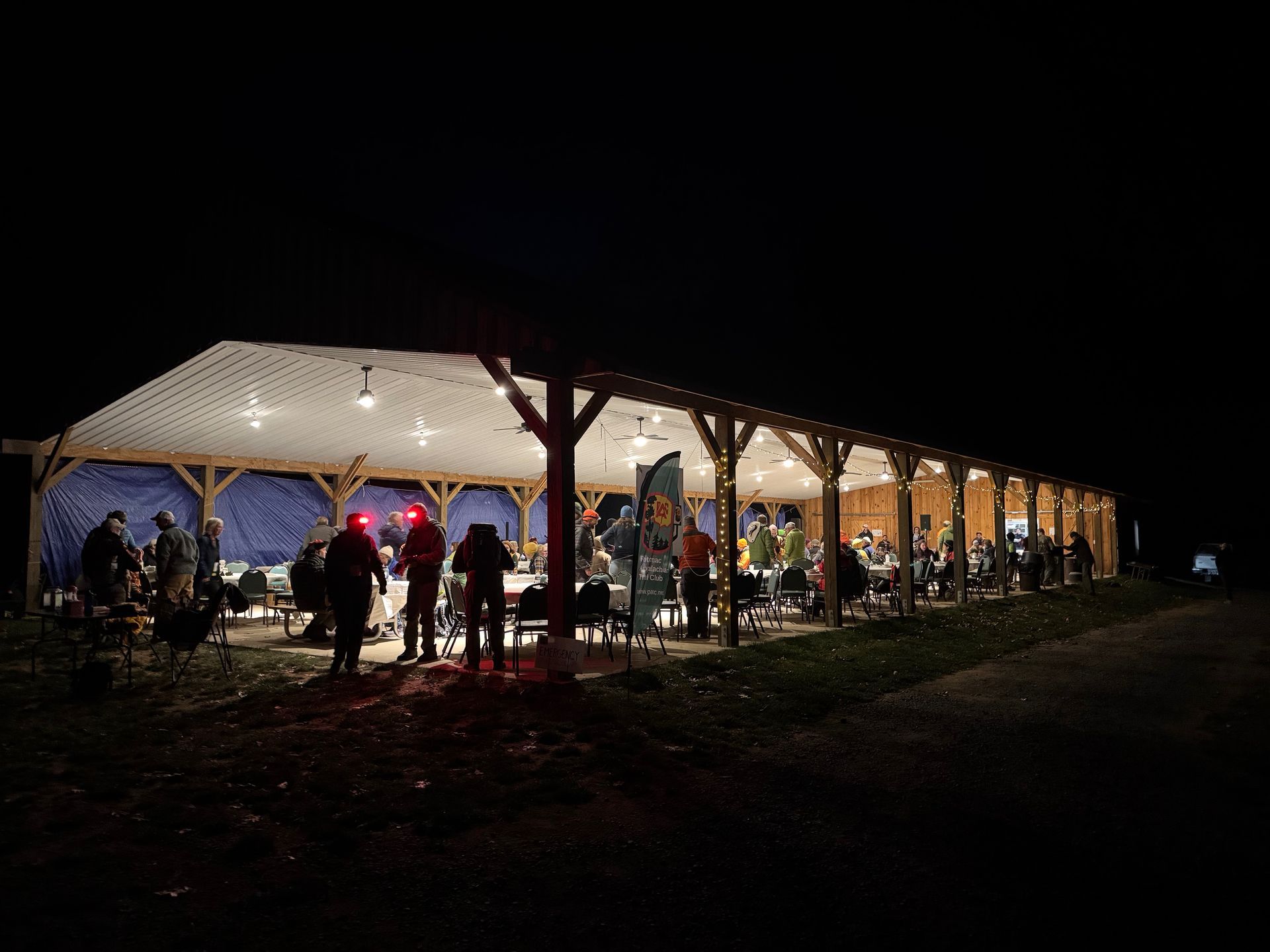 A group of people are standing under a tent at night.