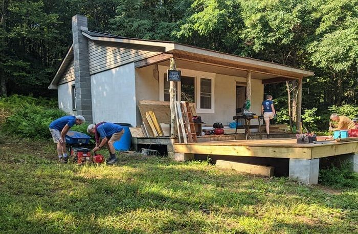 A group of people are working on a small house in the woods.