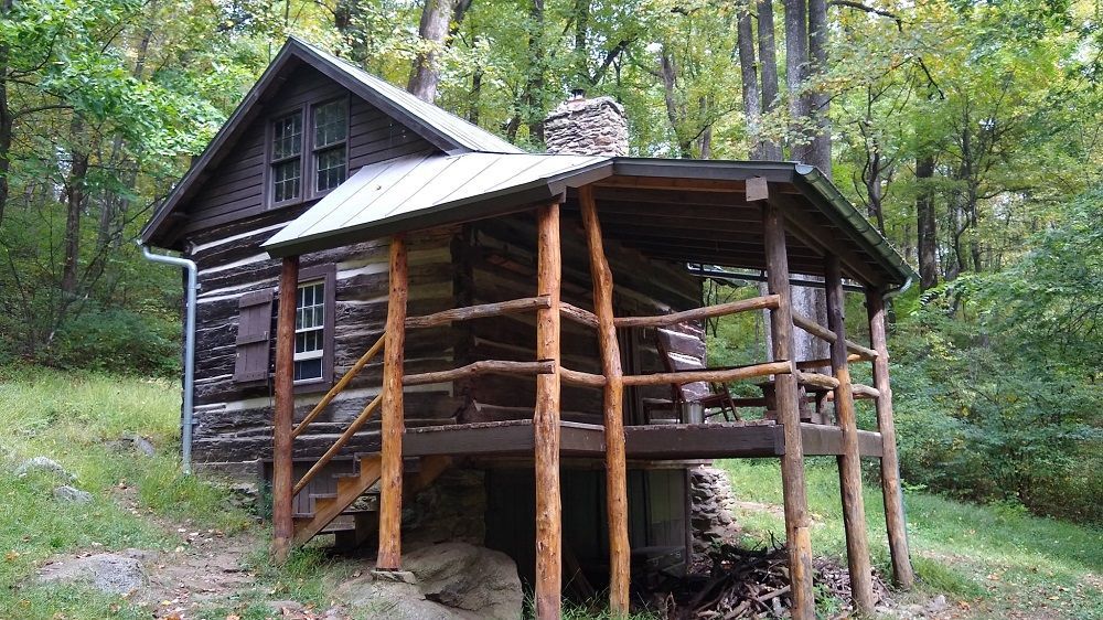 A small log cabin with a porch in the woods.