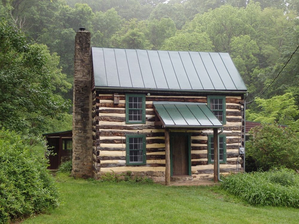 A log cabin with a green roof is surrounded by trees