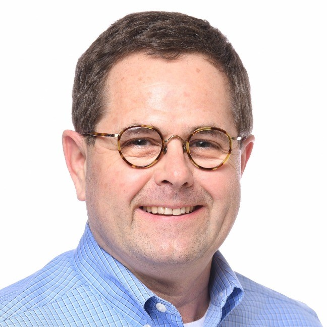 A man wearing glasses and a blue shirt smiles for the camera