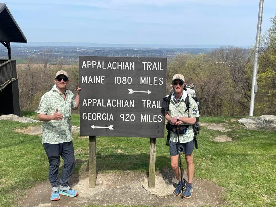 Two men are standing in front of a sign that says appalachian trail.