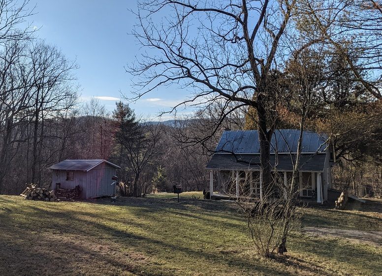A house with a porch and a shed in the middle of a field.