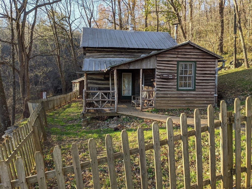 A log cabin with a porch and a wooden fence in the woods.