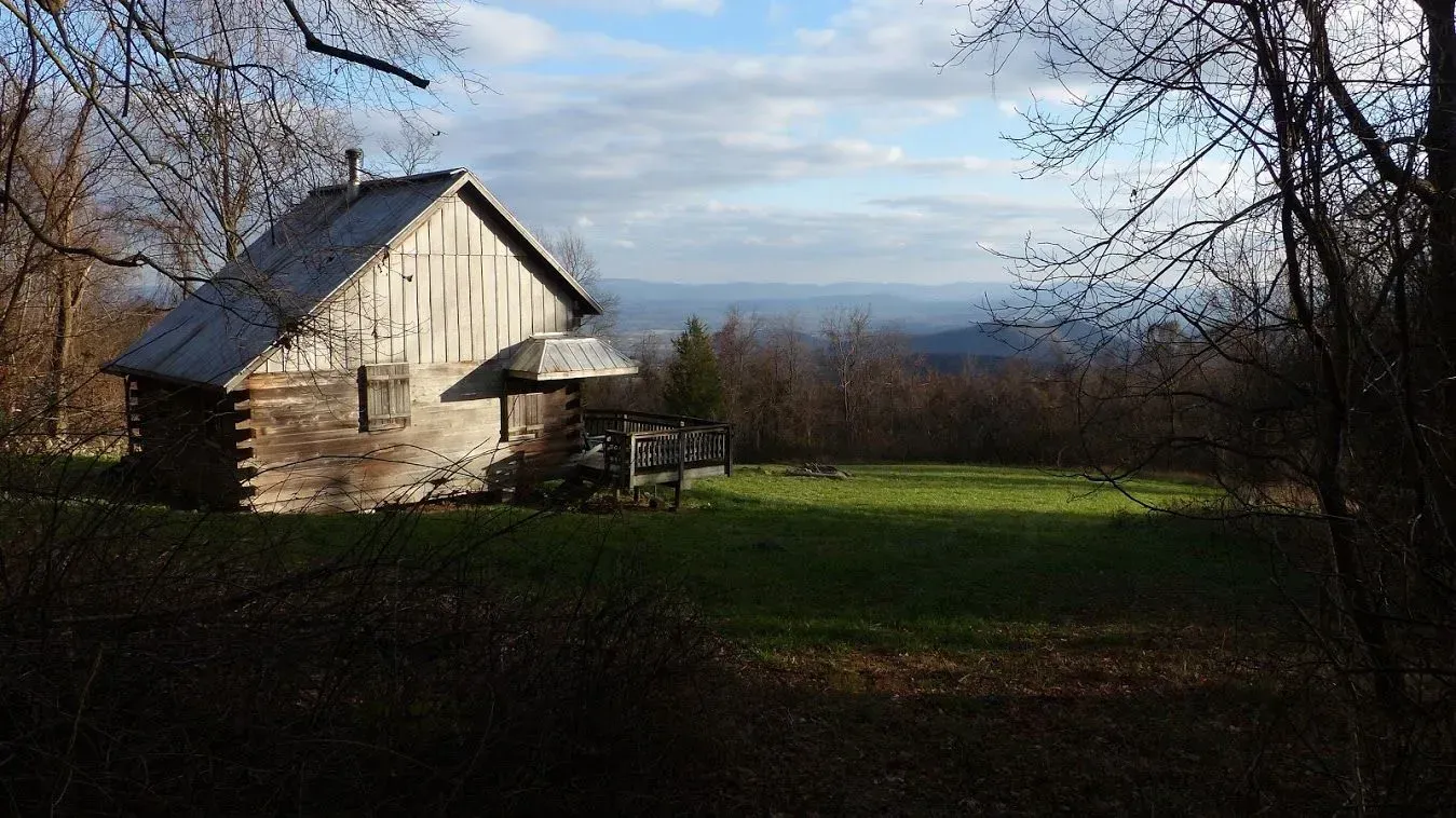 An old log cabin is sitting in the middle of a grassy field.