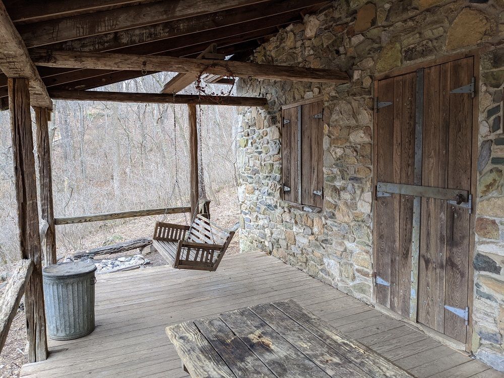 There is a porch with a wooden table and chairs on it.
