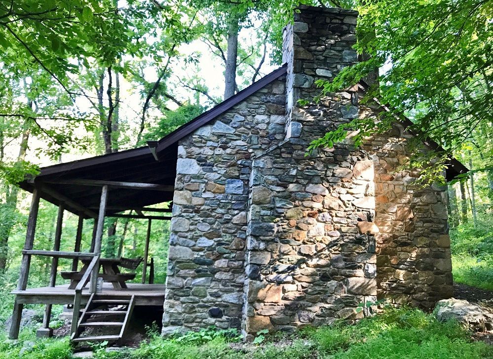 A small stone cabin with a picnic table and stairs in the woods.