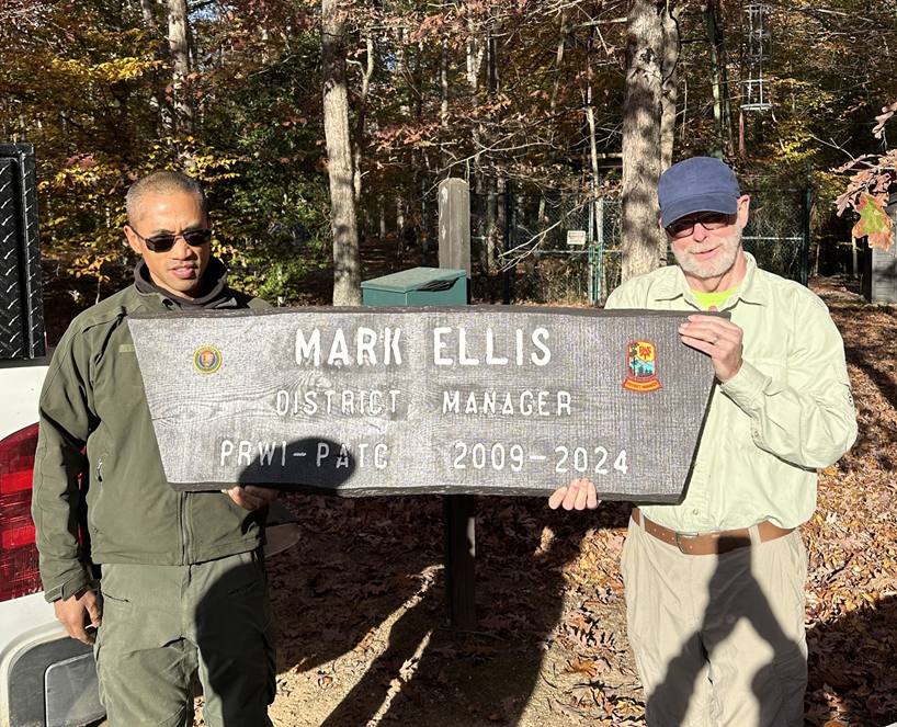 Two men are holding a sign that says mark ellis district manager