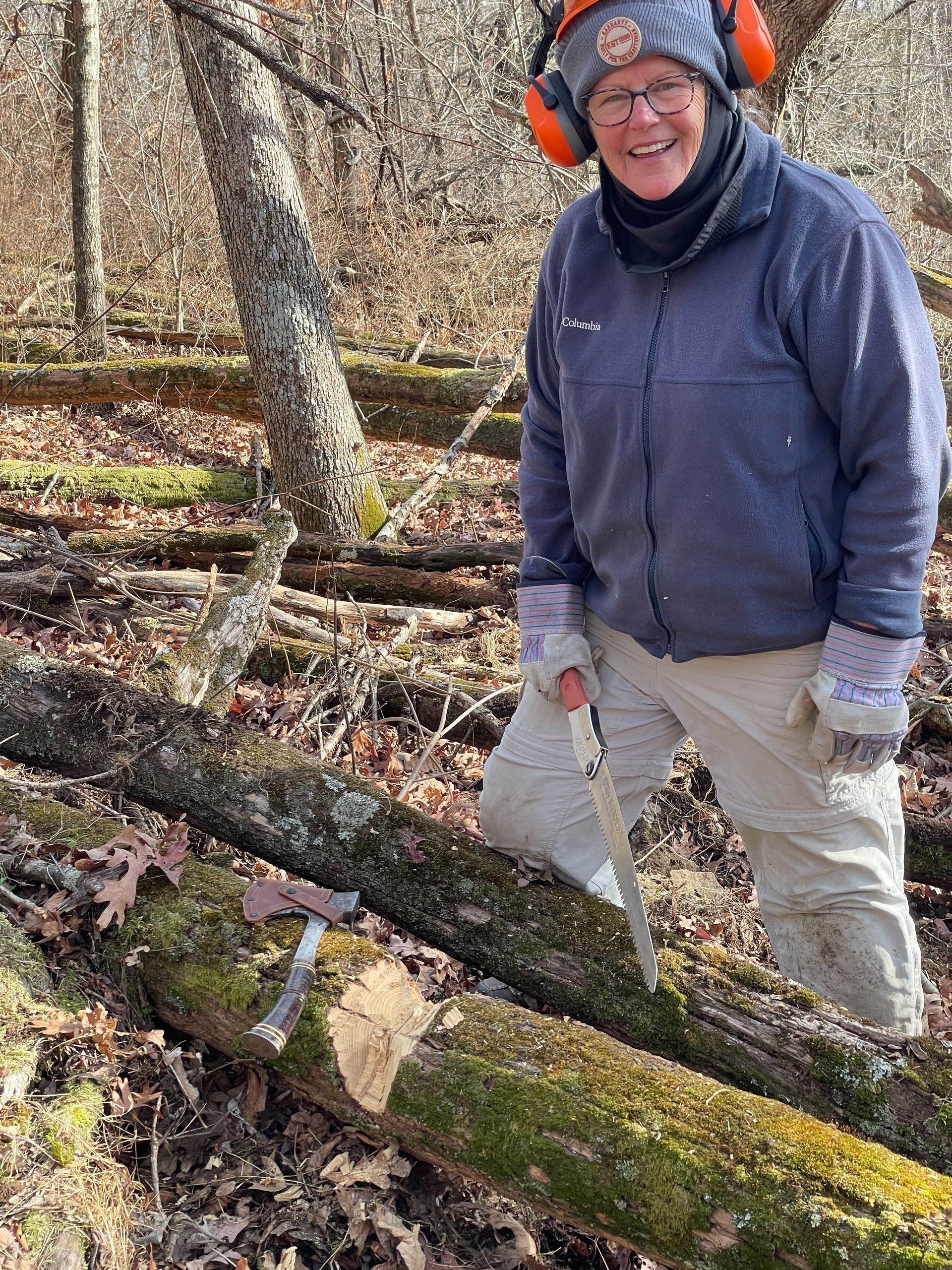 A woman is cutting a log with a saw in the woods.