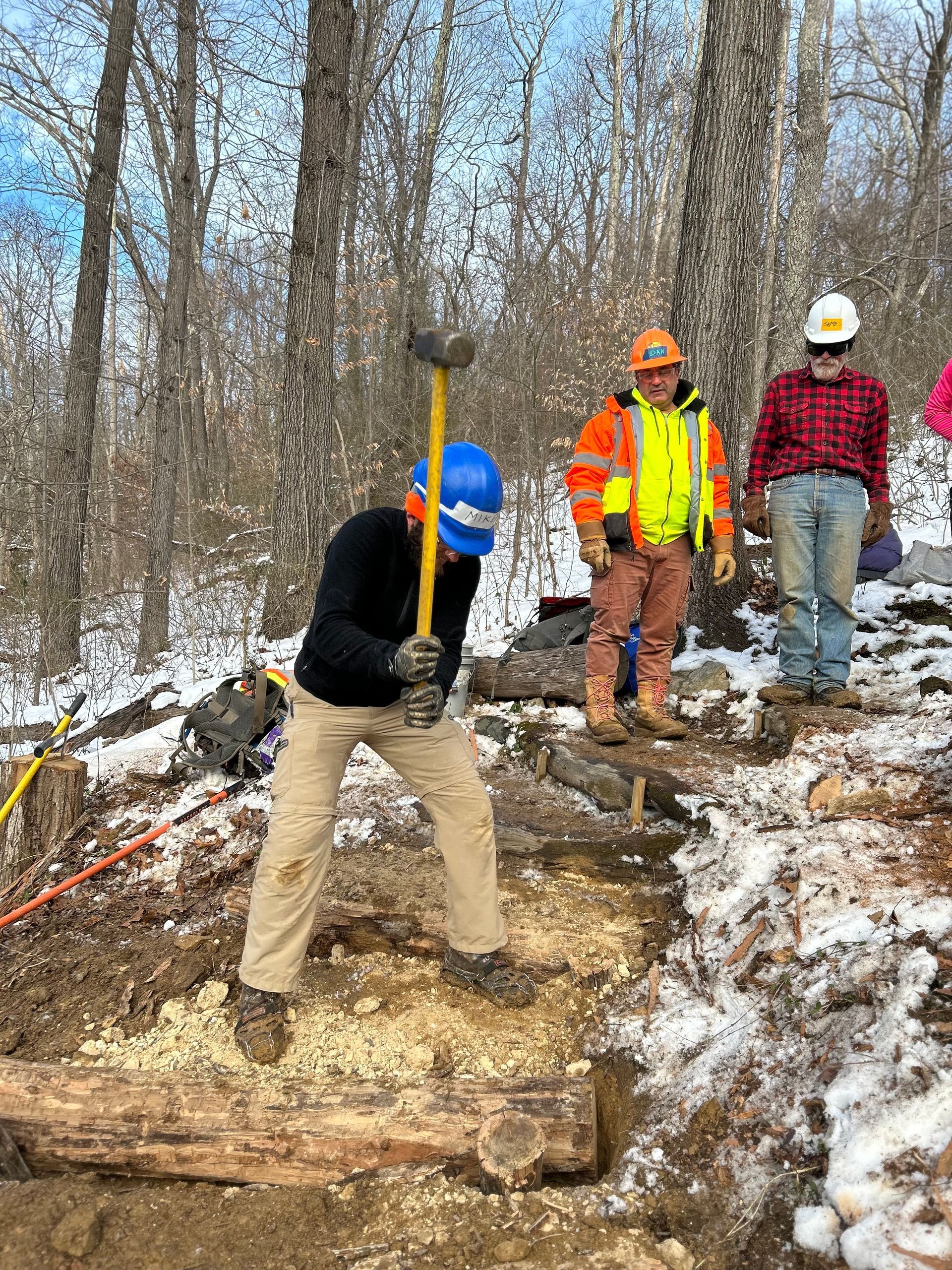 A man is using a hammer to break a log in the woods.