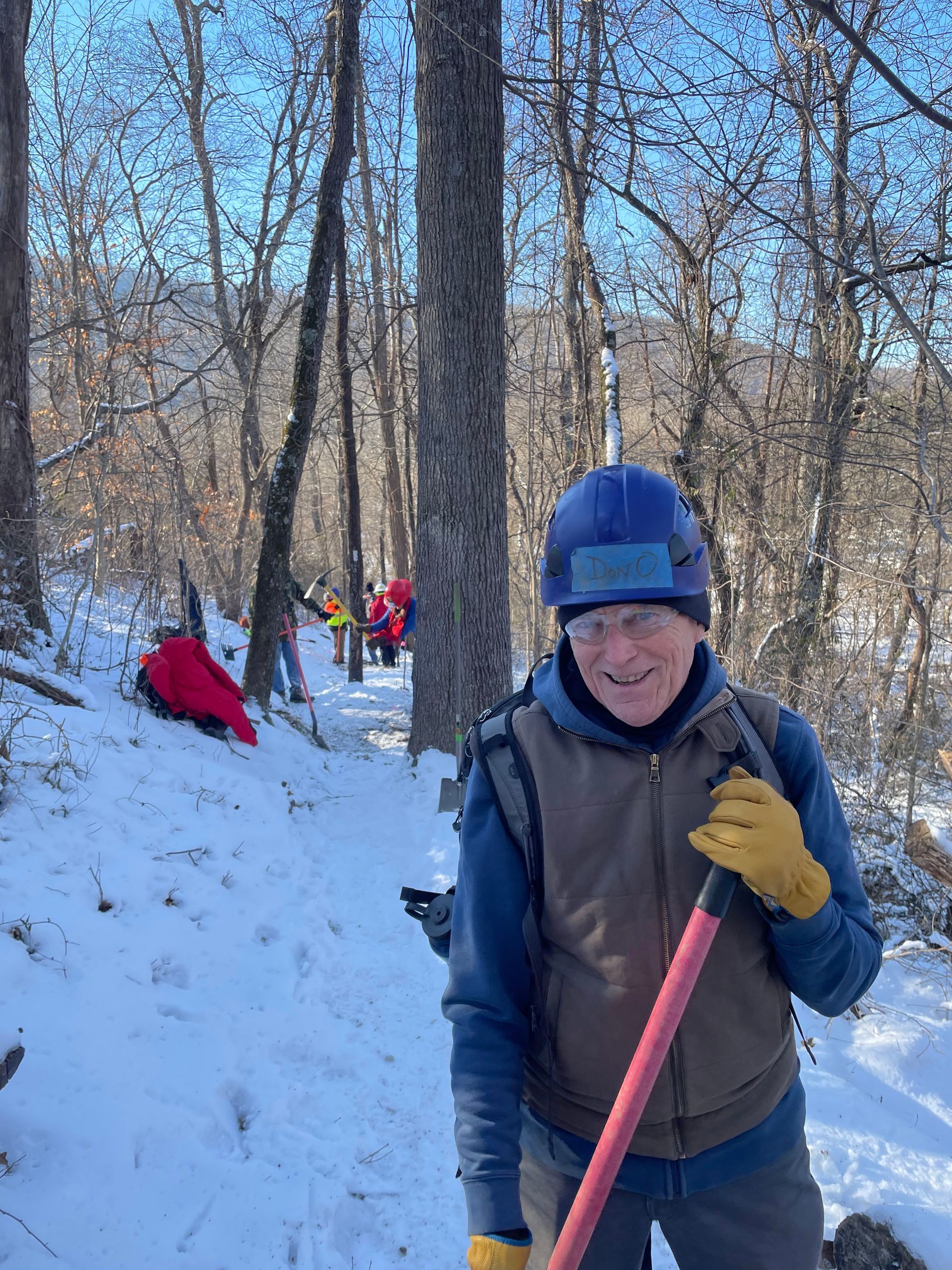 A man is standing in the snow holding a shovel.