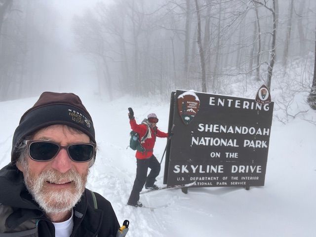 A man is standing in front of a sign that says entering shenandoah national park on the skyline drive