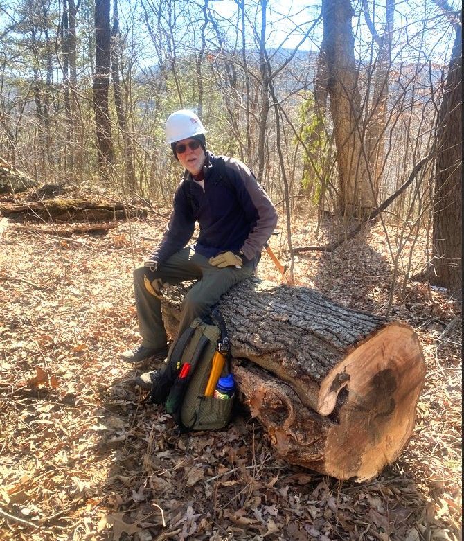 A man in a hard hat sits on a log in the woods
