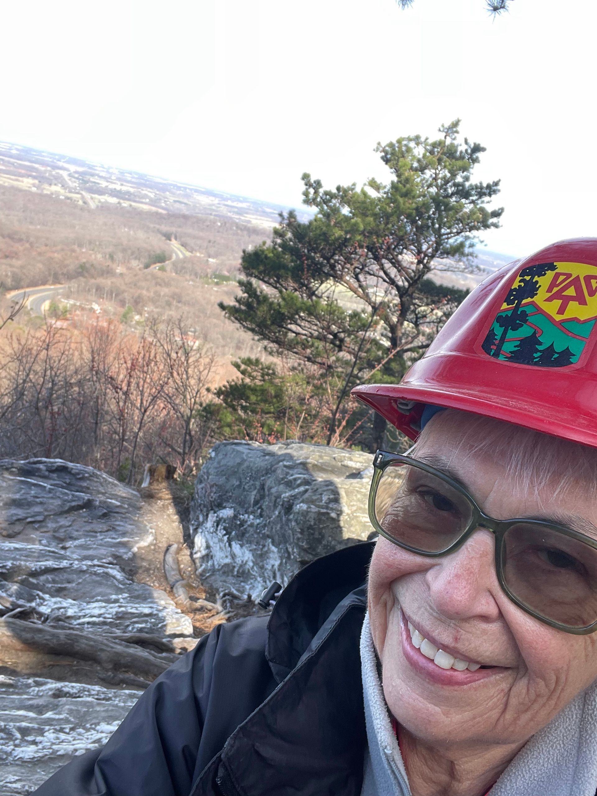 A woman wearing a red hard hat and sunglasses is smiling.