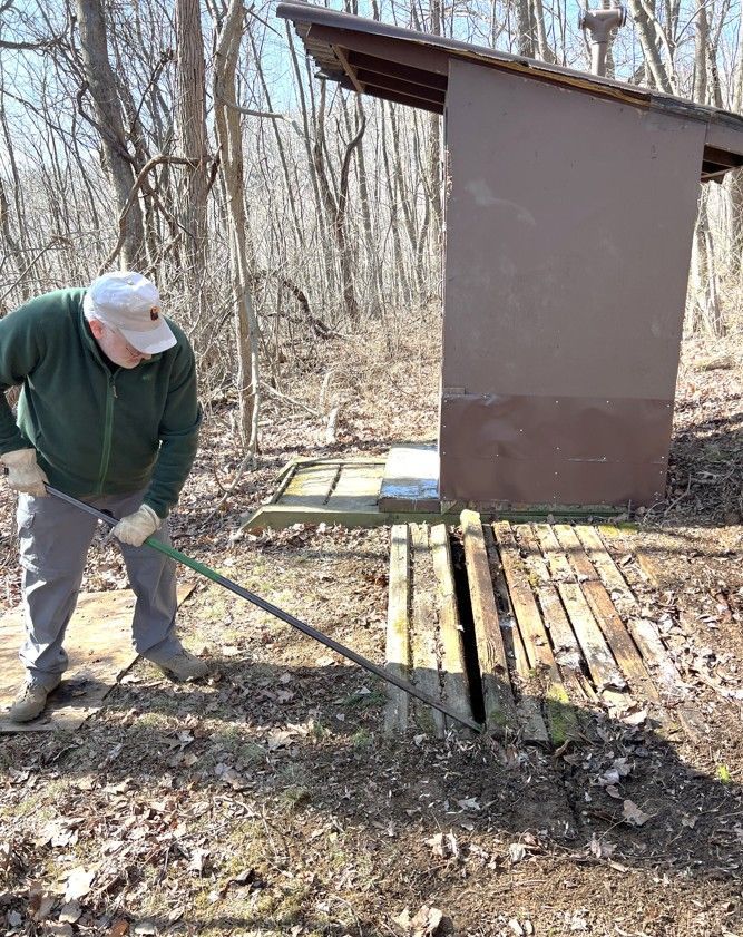 A man is standing next to a wooden shed in the woods.