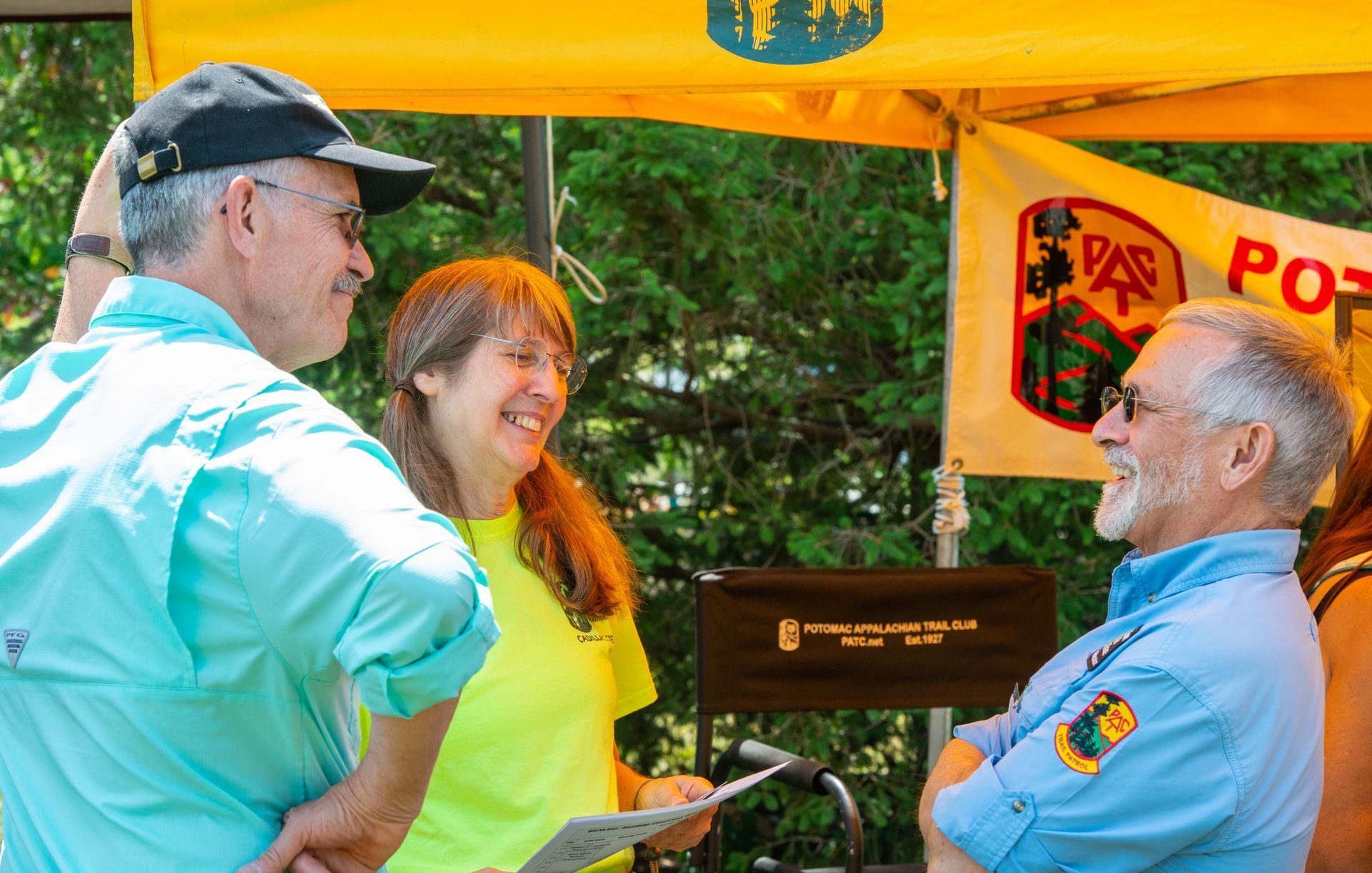 A group of people are standing under a yellow tent talking to each other.