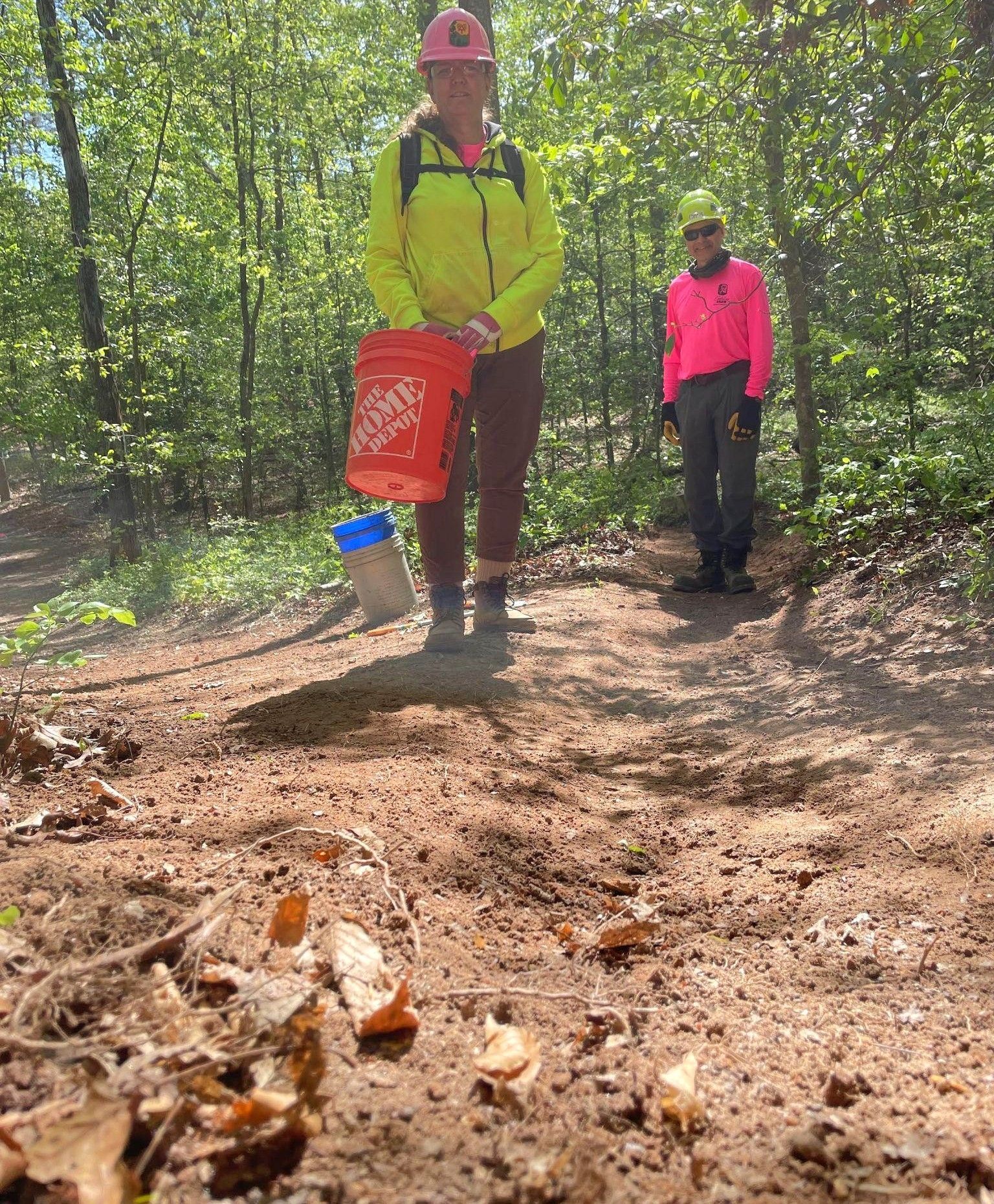 Two people are standing on a dirt path in the woods.
