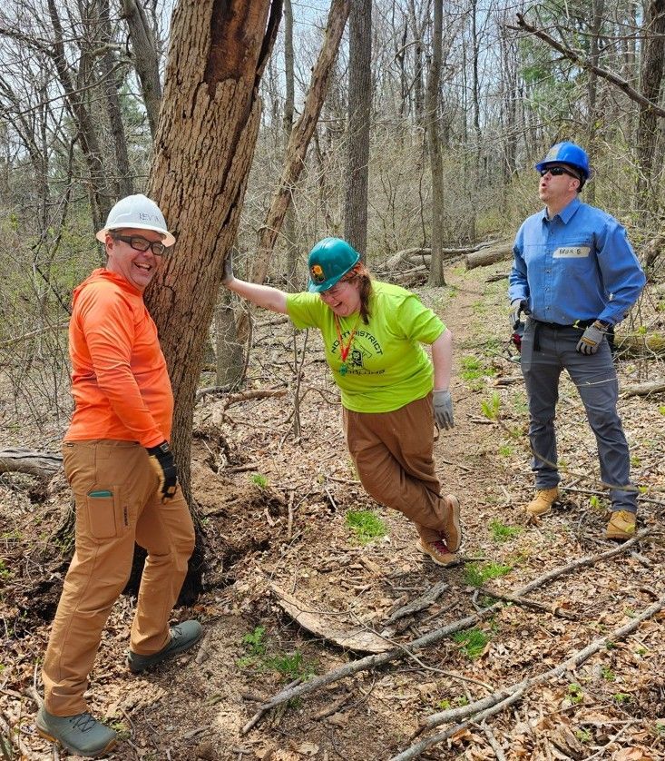 A group of people are standing next to a tree in the woods.