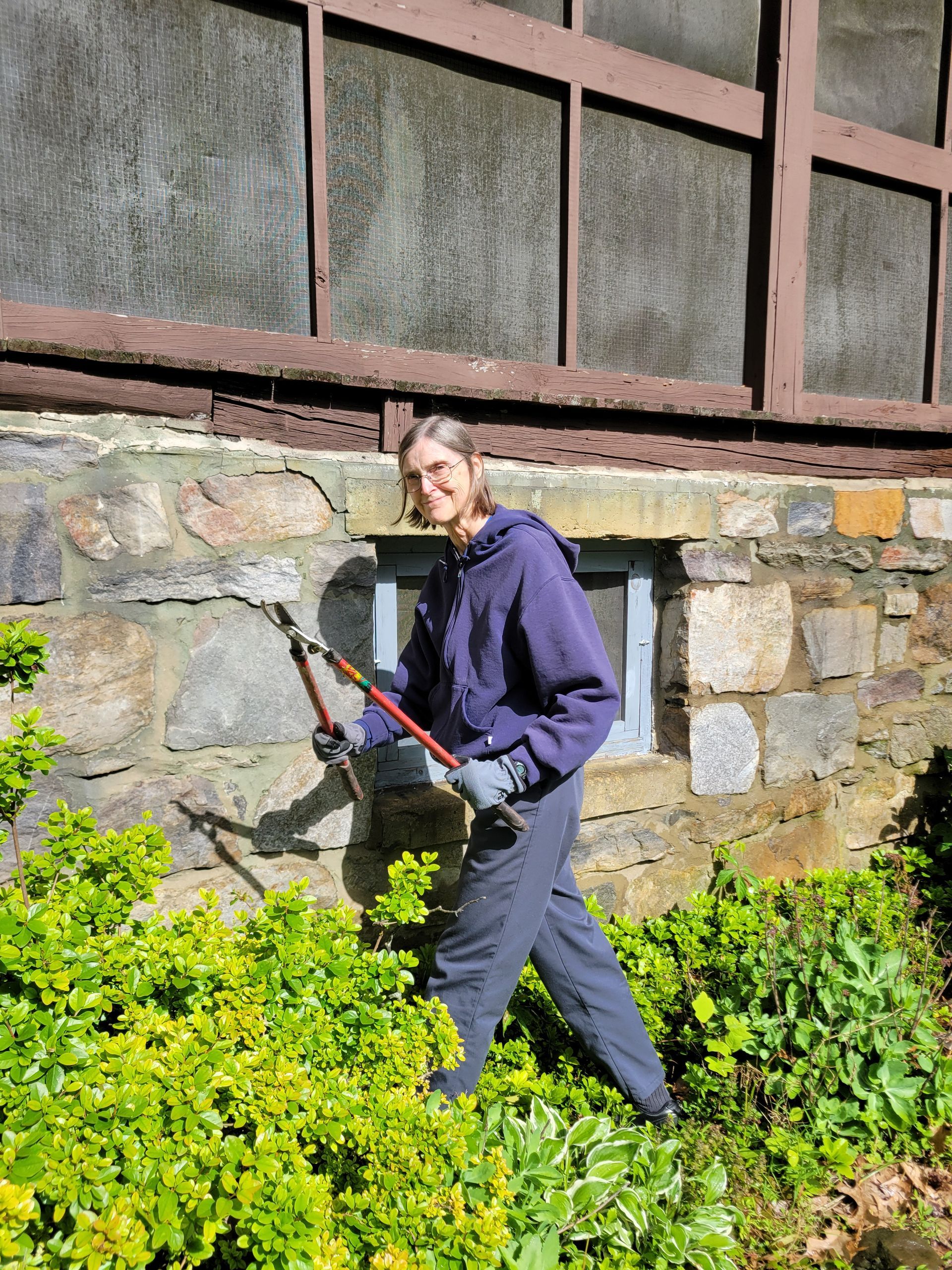 A woman is standing in front of a stone wall holding a pair of scissors.
