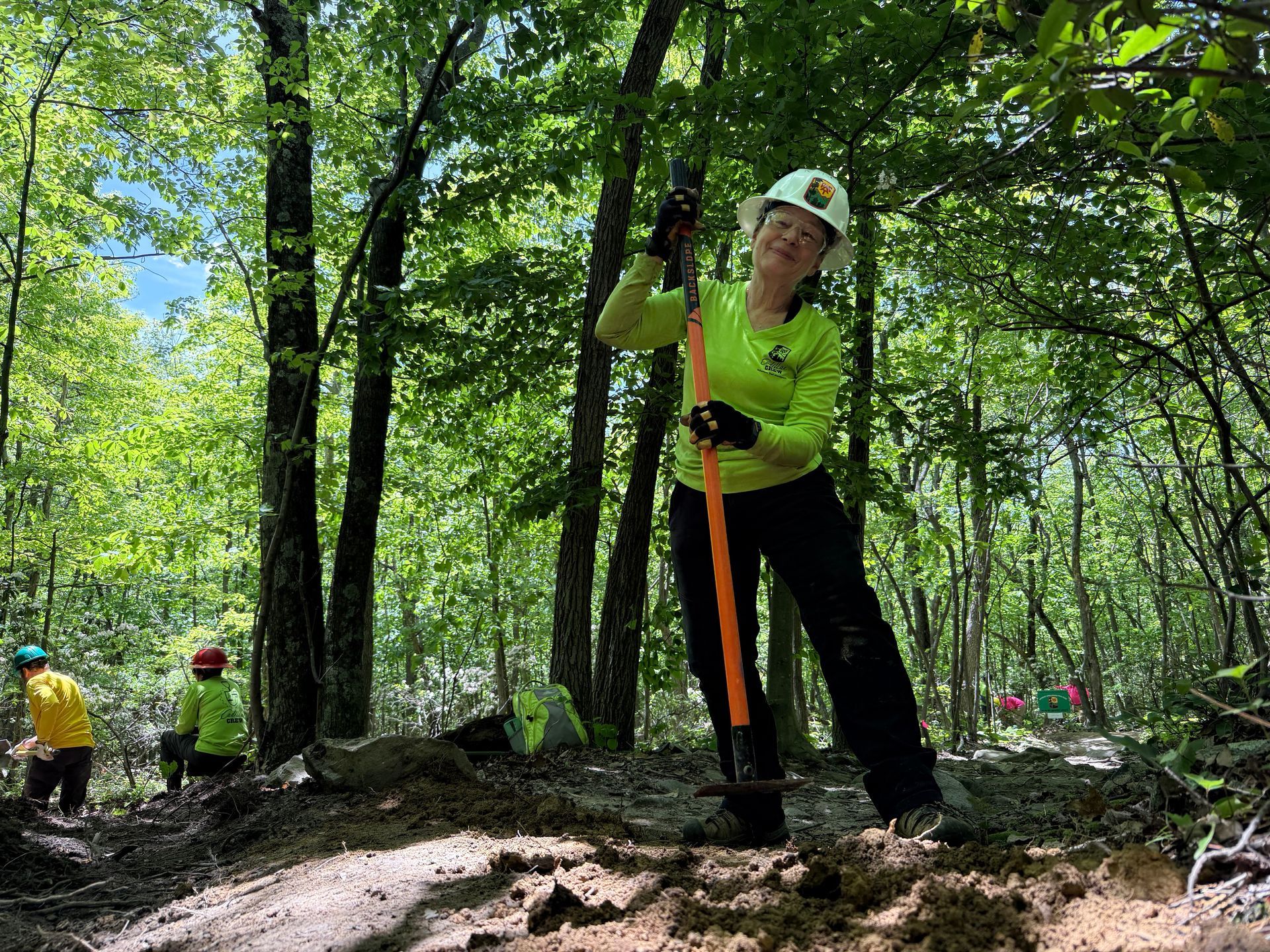 A woman is holding a shovel in the woods.