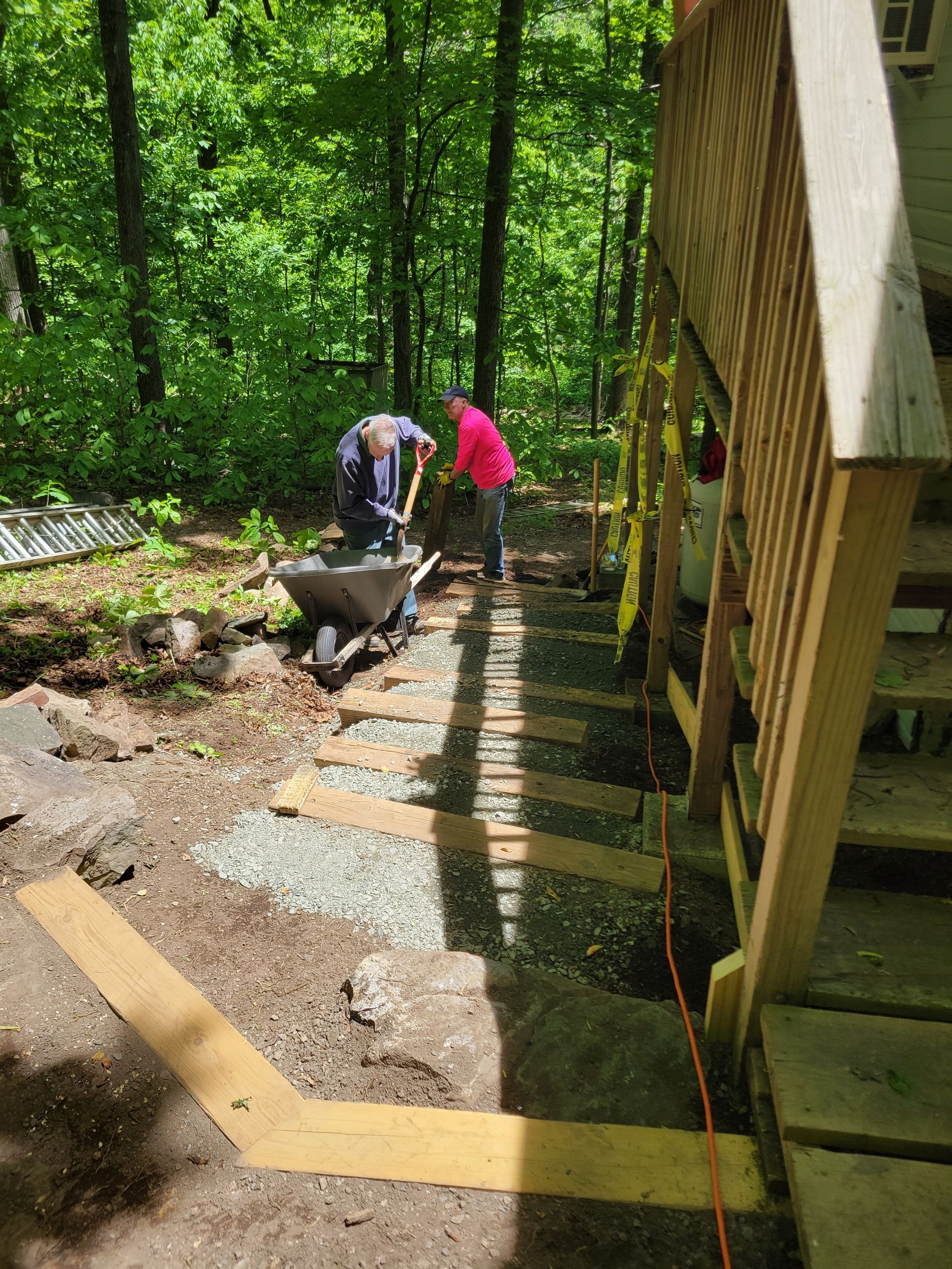 A man is pushing a wheelbarrow down a set of stairs in the woods.
