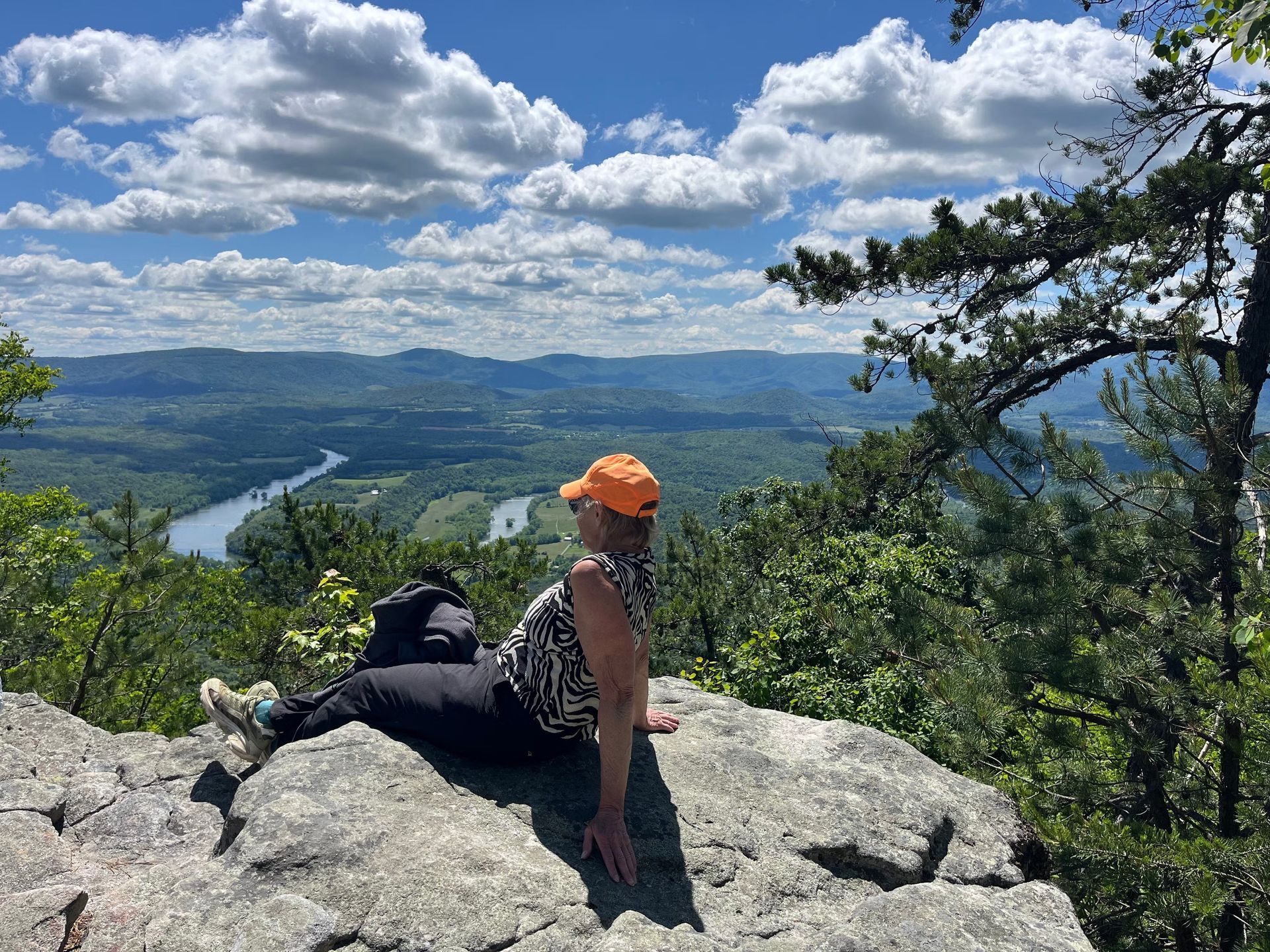 A woman is sitting on top of a rock overlooking a river.