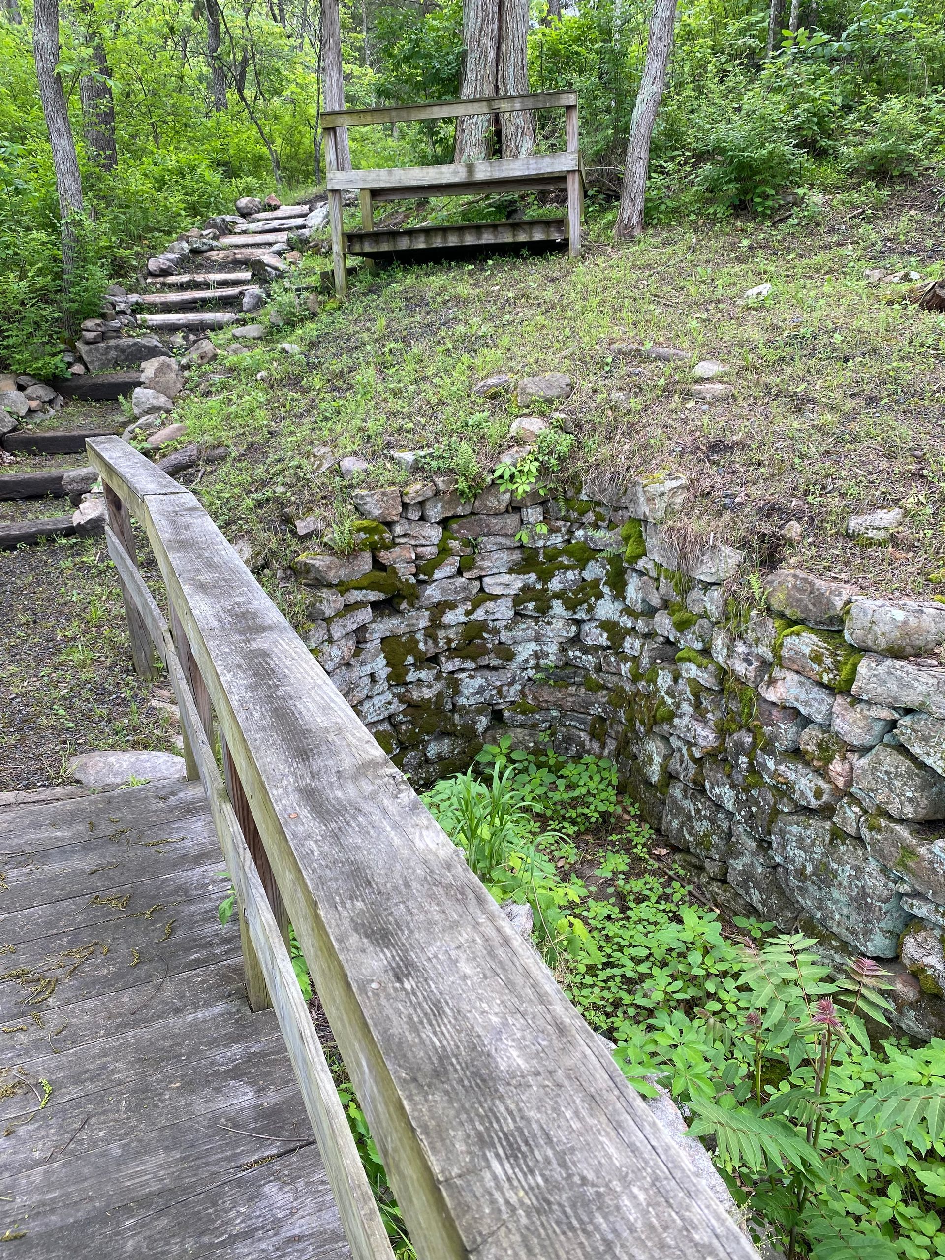 A wooden bridge leading to a stone wall in the woods.