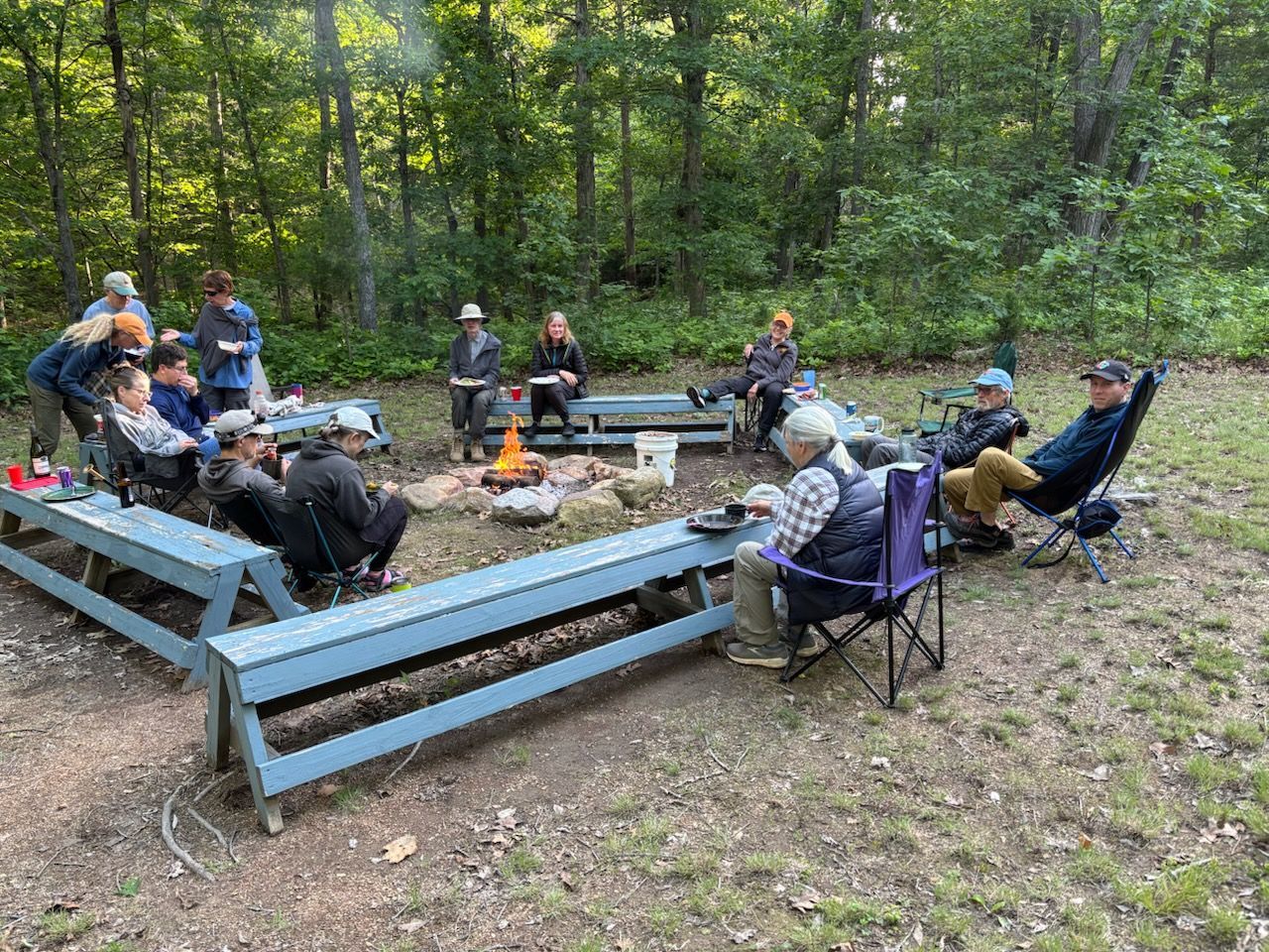 A group of people are sitting around a fire pit in the woods.