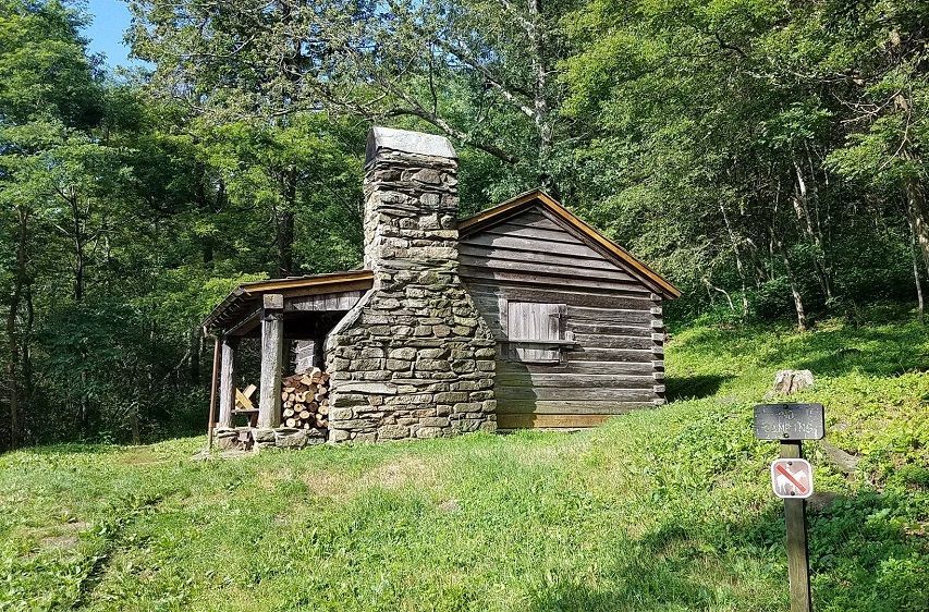 A small log cabin with a stone chimney in the middle of a forest.