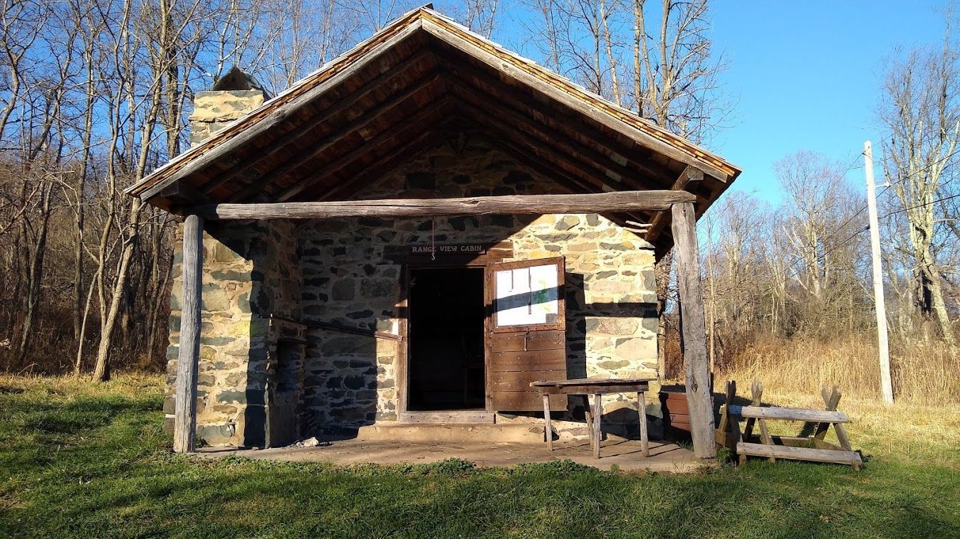 A small stone cabin with a porch in the middle of a field.