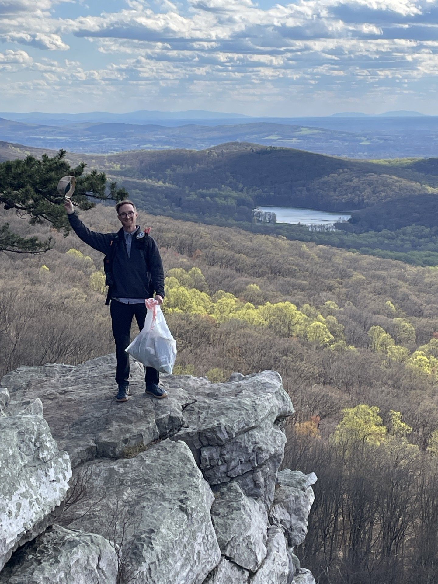 A man is standing on top of a rocky cliff holding a bag.