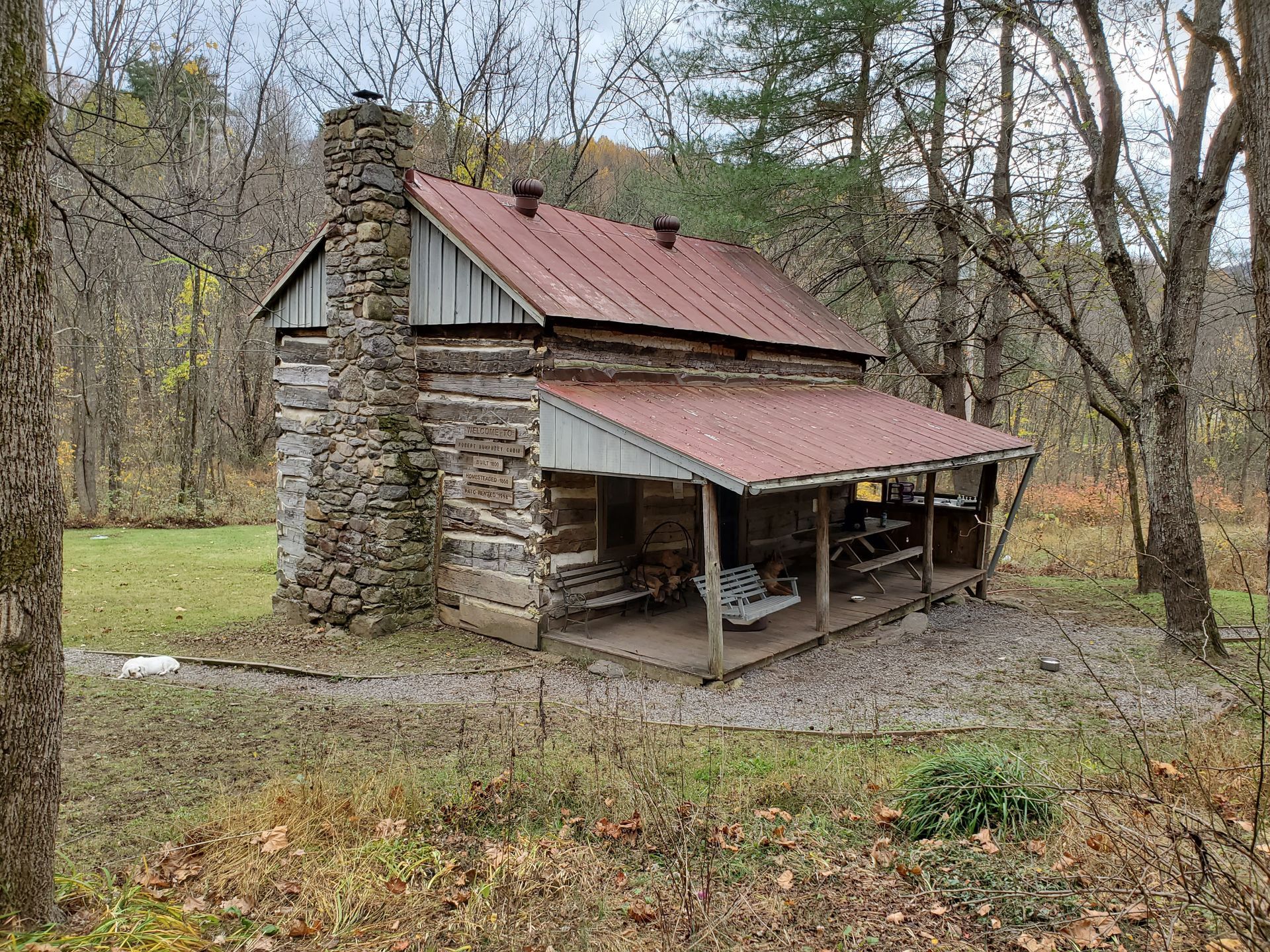 A small log cabin with a porch in the middle of a forest.