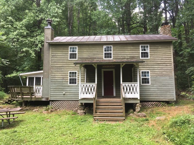 A house with a porch and stairs is in the middle of a forest.