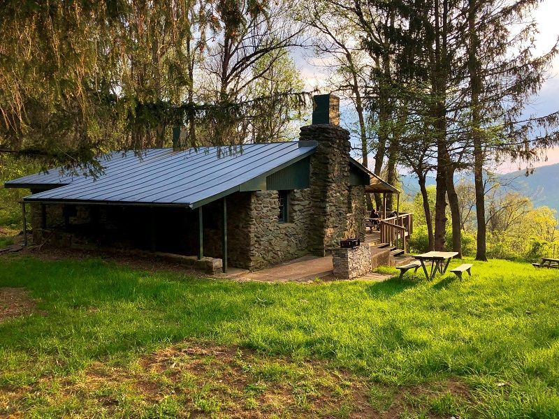 A stone cabin with a picnic table in front of it in the woods.
