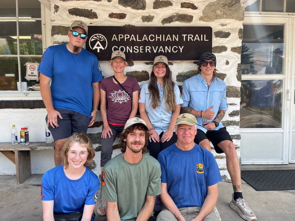 A group of people are posing for a picture in front of the appalachian trail conservancy.