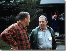 Two men are standing next to each other and talking in front of a building.