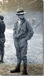 A man in a hat is standing in the dirt in a black and white photo.
