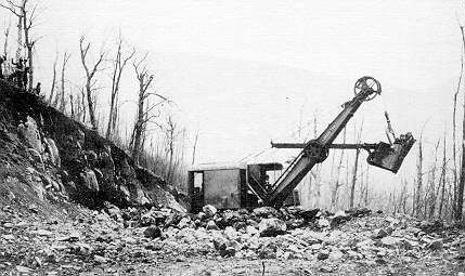 A black and white photo of an old excavator digging a hole in the ground.