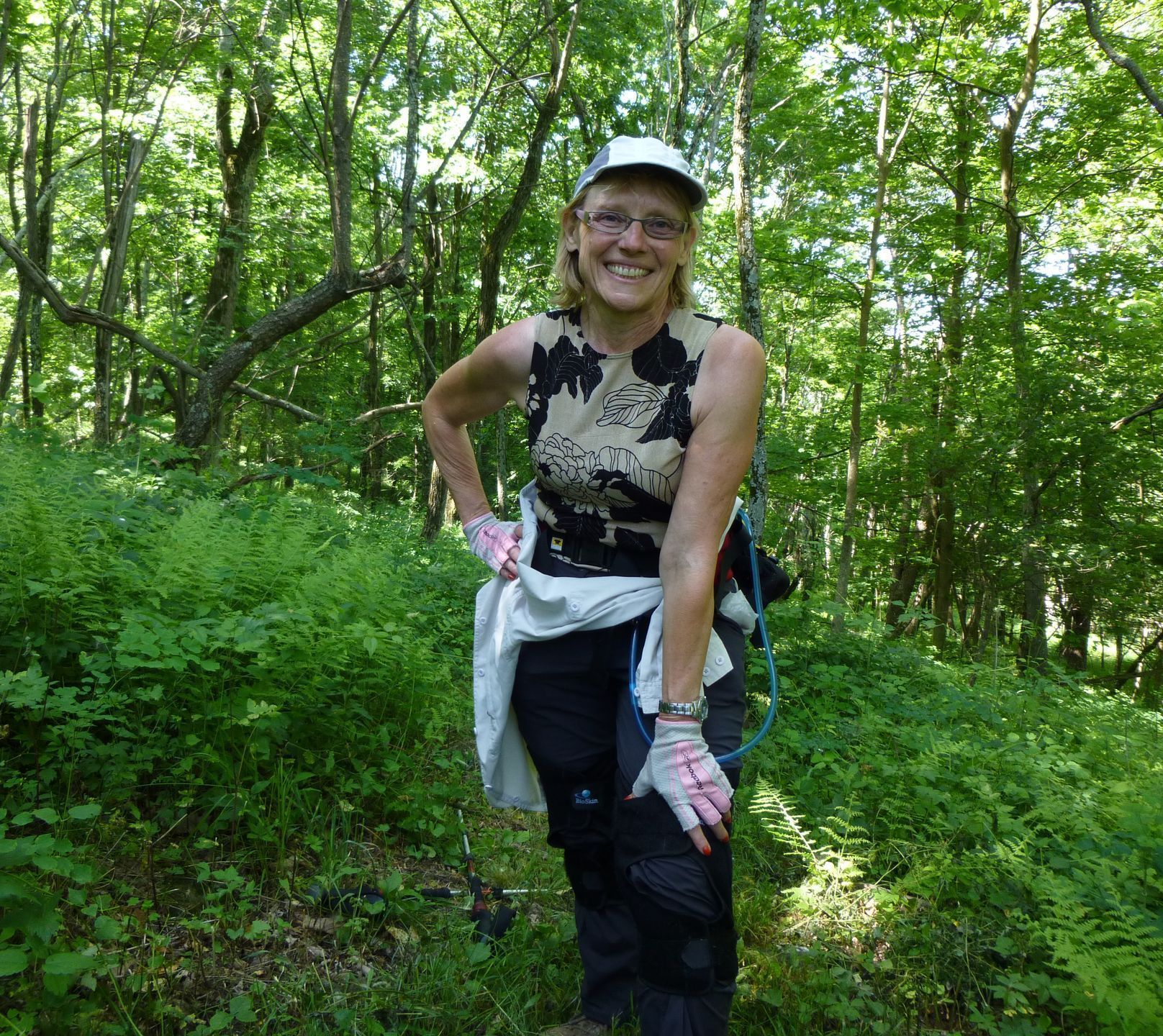 A woman wearing a hat and gloves is standing in the woods.