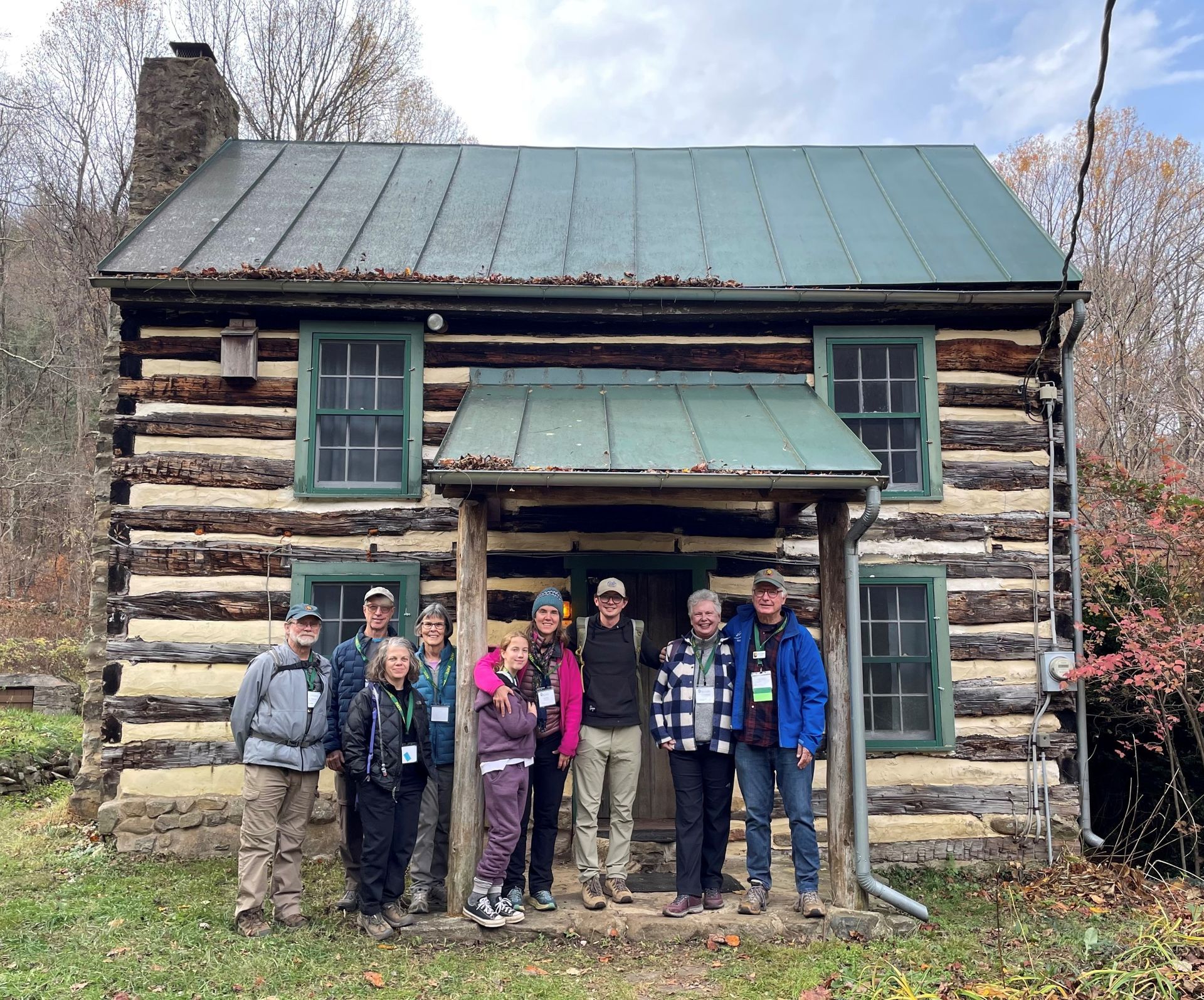 A group of people are standing in front of a log cabin.
