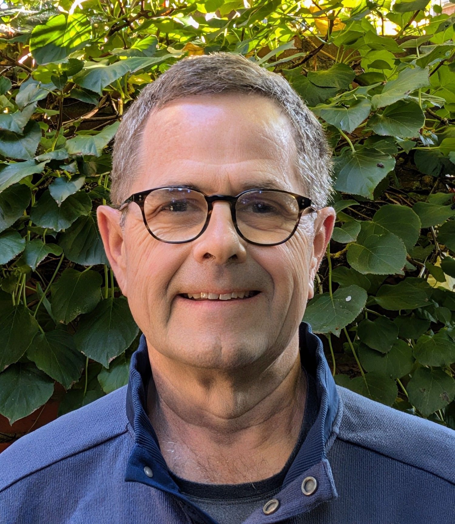 A man wearing glasses and a blue shirt smiles for the camera