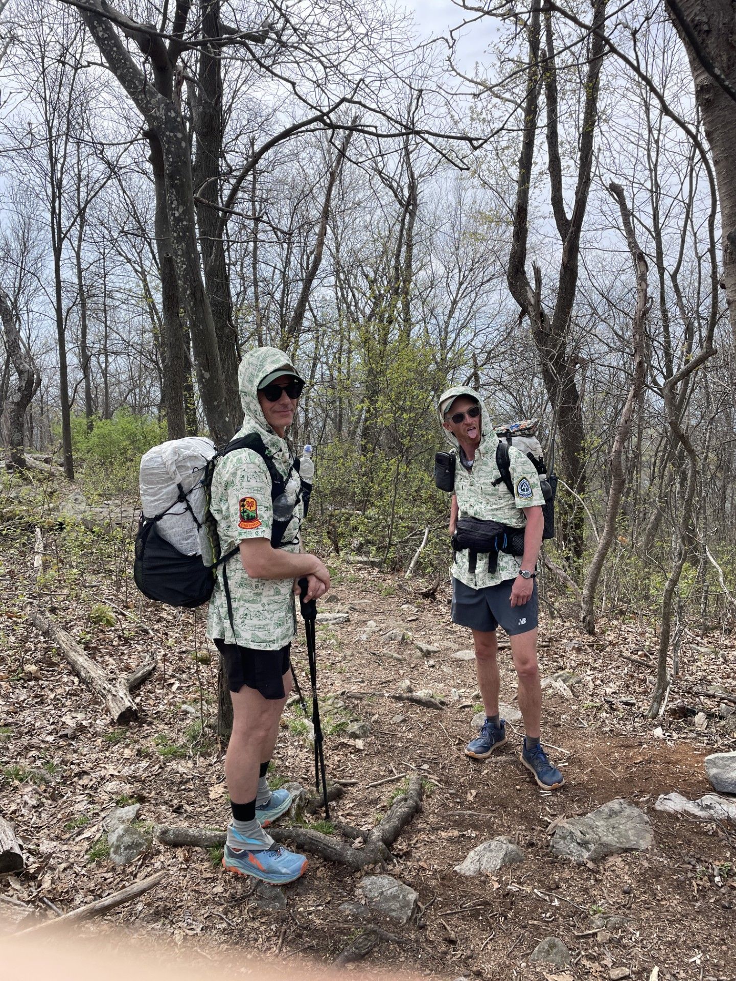 Two men with backpacks are standing in the woods.