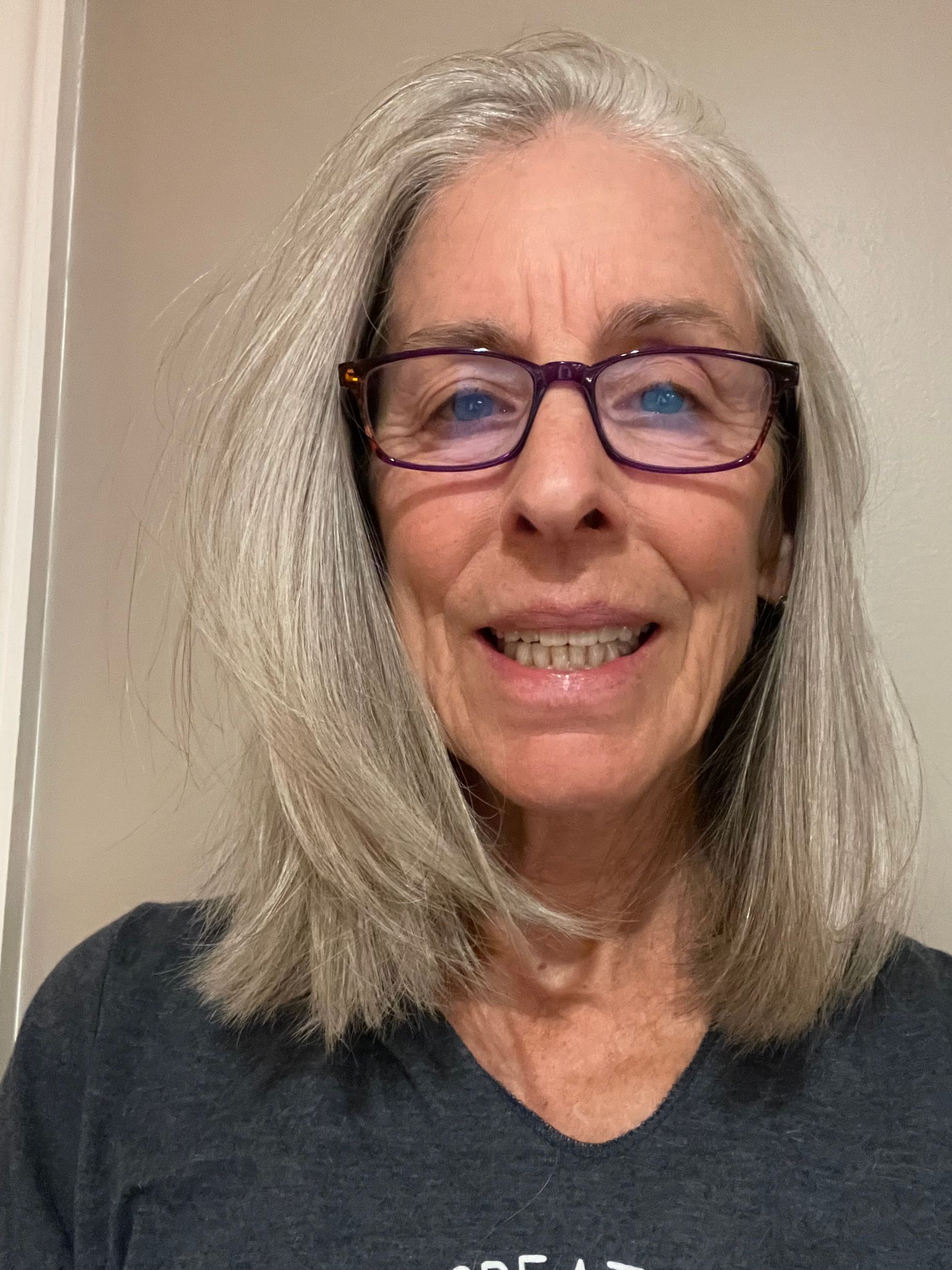 A woman with gray hair and glasses is smiling for the camera.