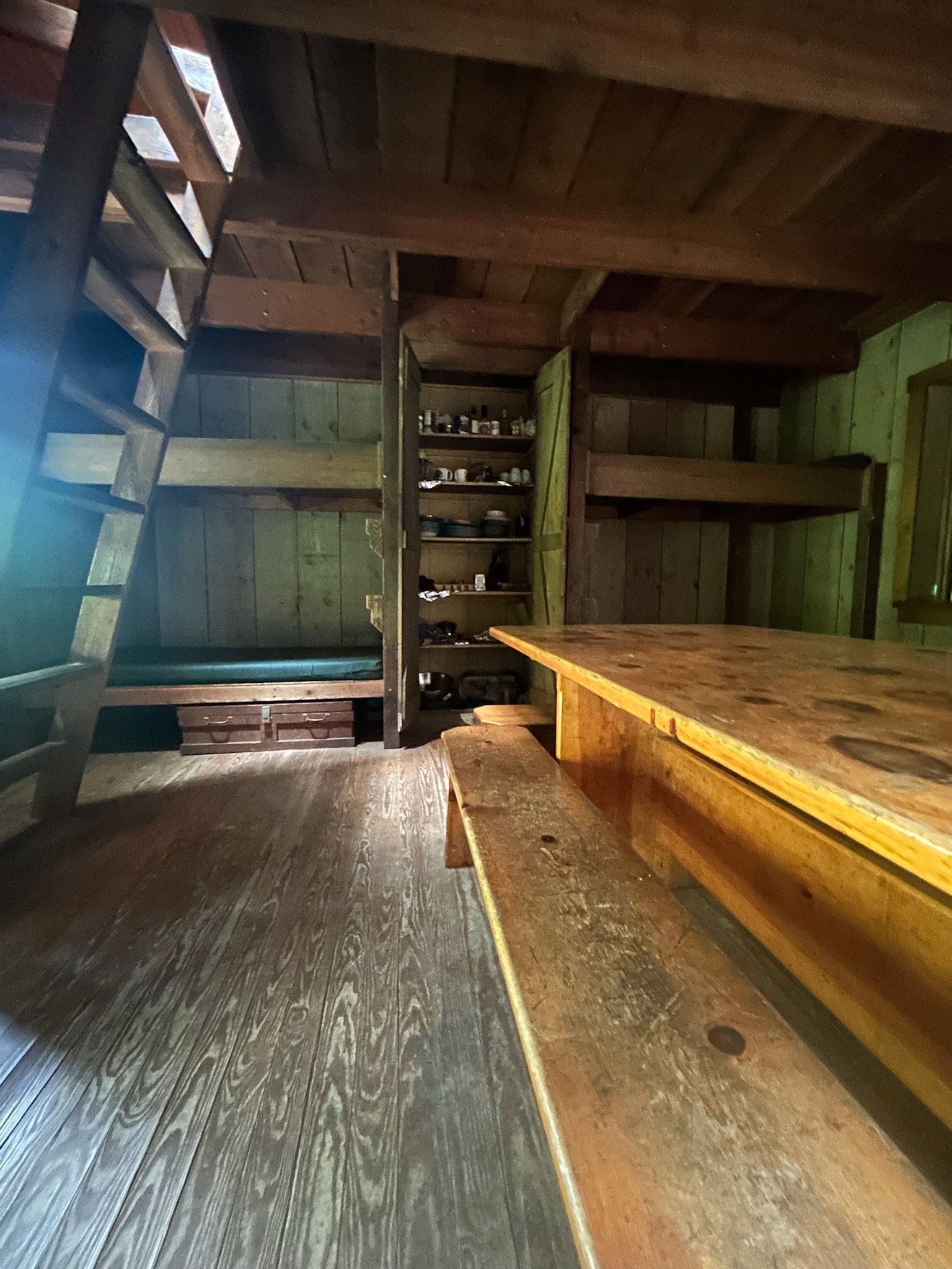 A wooden room with bunk beds , a table and benches.