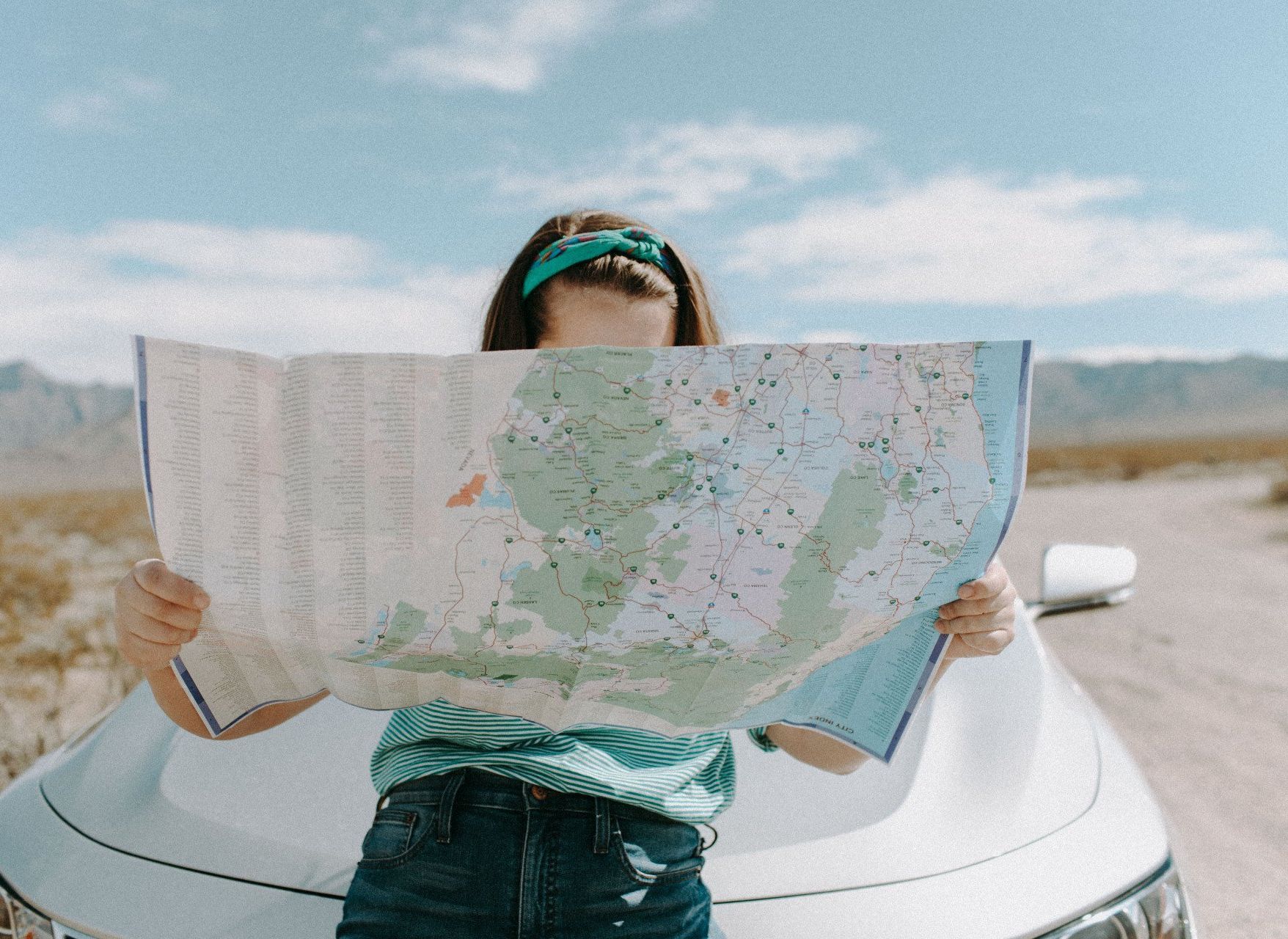 A woman is standing next to a car holding a map.